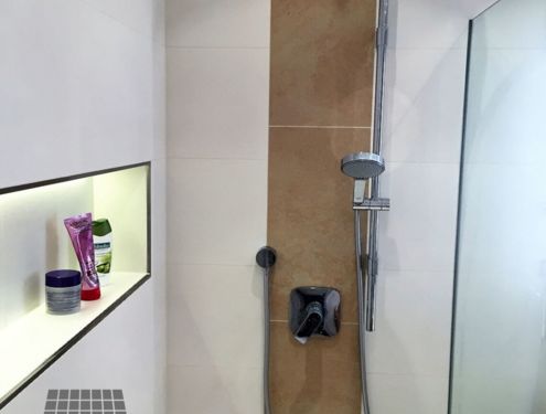 Zeitloses Badezimmer mit Dekorstreifen an der Duschrückwand und Duschnische für Shampoo etc.
