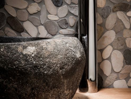 Nahaufnahme von einem Natursteinwaschbecken mit Steinverkleidung an der Wand im Hintergrund