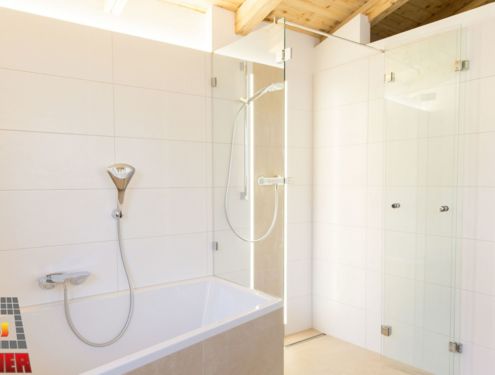 Helles Badezimmer mit Holzdecke, sandfarbenen und weißen Fliesen, barrierefreier Dusche und indirekter Beleuchtung für noch mehr Gemütlichkeit.