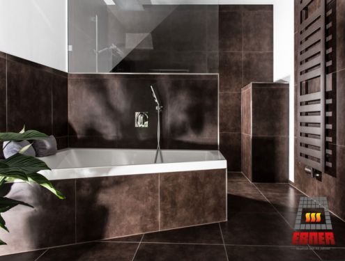 Modernes und stilvolles Badezimmer, welches durch seine dunklen Fliesen und den schlicht gehaltenen Möbelstücken in Holz zeitlos ist.