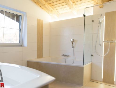 Helles Badezimmer mit Holzdecke, sandfarbenen und weißen Fliesen, barrierefreier Dusche und indirekter Beleuchtung für noch mehr Gemütlichkeit.