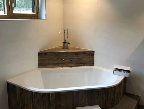 Badewanne mit Ablagefläche in dunklen Holzoptikfliesen verkleidet.