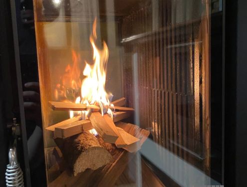 Ein kleiner Tischherd auf Dekorfliese mit eingebauter Holzlade und Sichtfenster für besondere Stimmung beim Kochen.