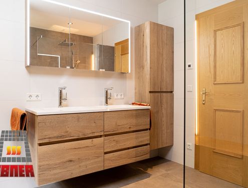 Modern, zeitlos und im Landhausstil. Durch die schlichten Fliesenfarben und den Badezimmermöbeln aus Holz wirkt das Badezimmer gemütlich und freundlich.