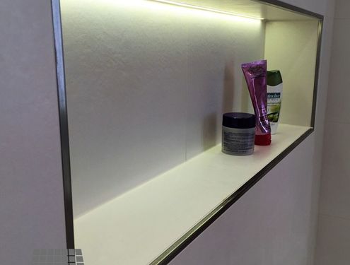 Zeitloses Badezimmer mit Dekorstreifen an der Duschrückwand und Duschnische für Shampoo etc.