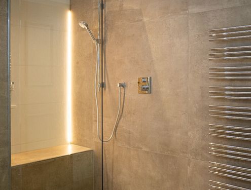 Modern, zeitlos und im Landhausstil. Durch die schlichten Fliesenfarben und den Badezimmermöbeln aus Holz wirkt das Badezimmer gemütlich und freundlich.