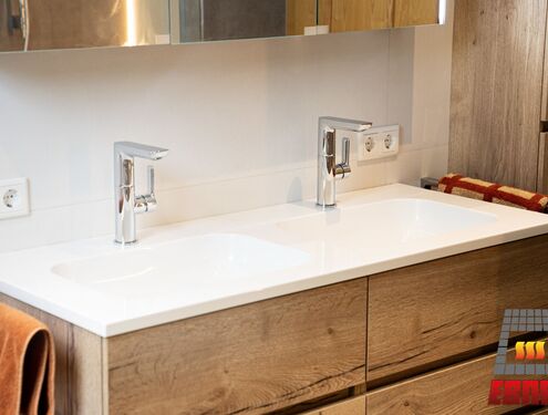 Modern, zeitlos und im Landhausstil. Durch die schlichten Fliesenfarben und den Badezimmermöbeln aus Holz wirkt das Badezimmer gemütlich und freundlich.