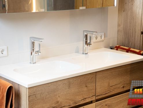 Modern, zeitlos und im Landhausstil. Durch die schlichten Fliesenfarben und den Badezimmermöbeln aus Holz wirkt das Badezimmer gemütlich und freundlich.