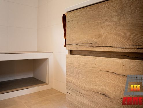 Modern, zeitlos und im Landhausstil. Durch die schlichten Fliesenfarben und den Badezimmermöbeln aus Holz wirkt das Badezimmer gemütlich und freundlich.